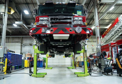 A red and black fire truck on lifts on a manufacturing floor.