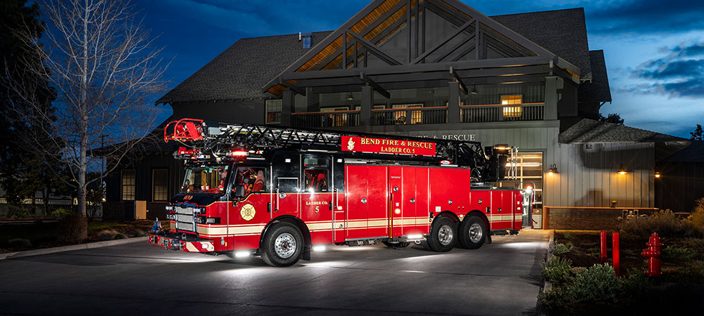 Velocity Ascendant 107 Aerial Ladder parked in front of firehouse at dusk.