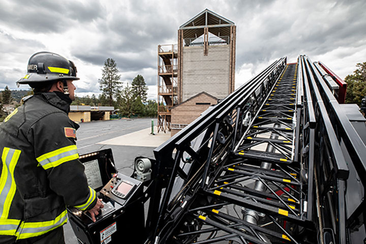 Firefighter operating an aerial ladder fire truck on a cloudy day.