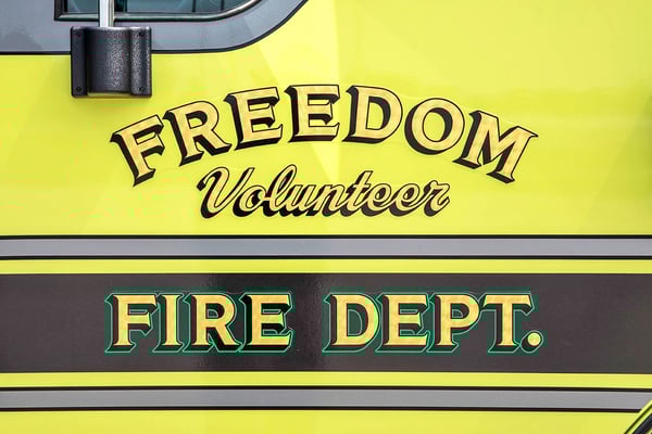 The drivers door of a yellow fire truck with graphics for Freedom Volunteer Fire Department.-1