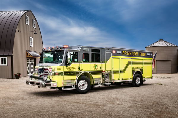 Thumbnail The front drivers side of a Velocity PUC Pumper parked by a barn on gravel on a partly cloudy day.