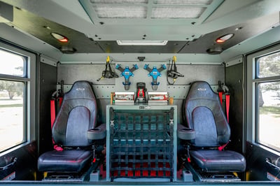 The crew cab of a fire truck with two seats, headsets and a compartment in the middle with a net cover.