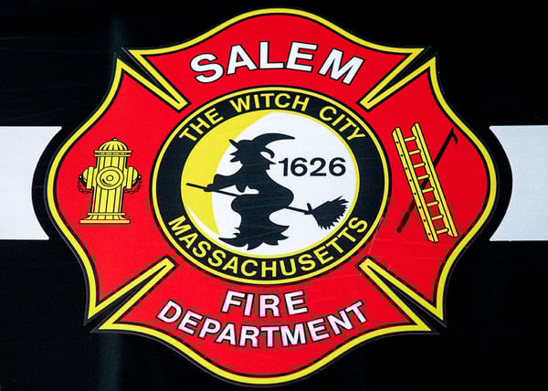 The maltese cross logo for Salem Fire Department with a witch flying on a broomstick in the center of the logo.