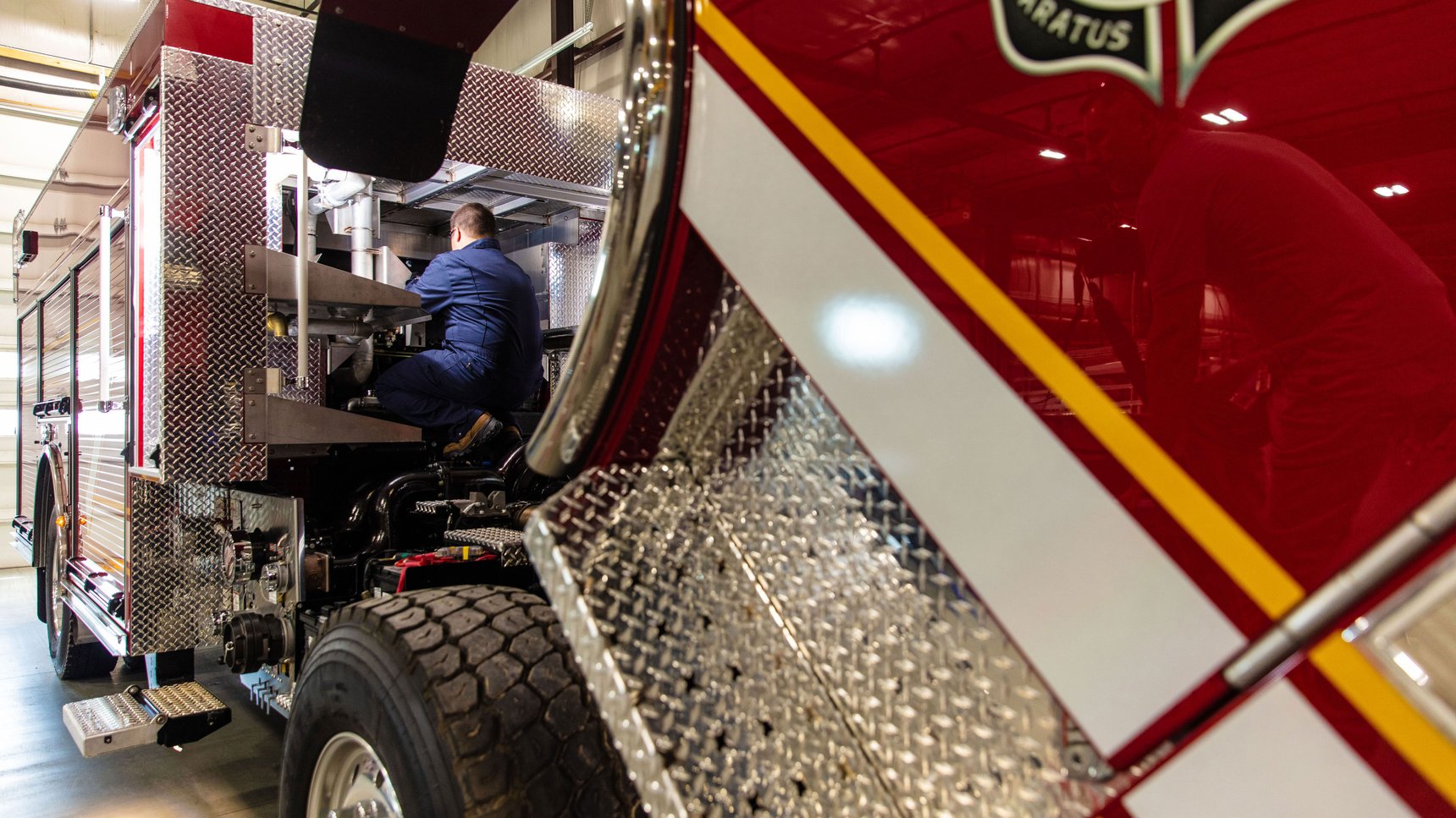 A red Pierce fire apparatus with service technician in a blue jumpsuit working on the apparatus.