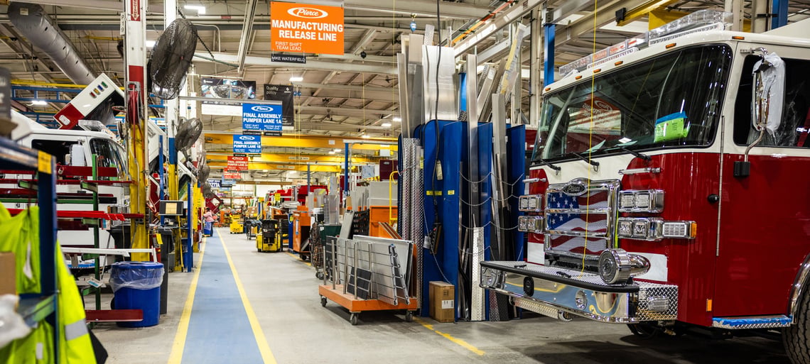 A fire truck manufactuting facility with fire trucks being built and parts on carts beside them.