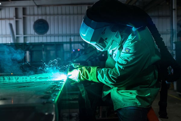 A fire truck welder in a welding suit working on welding a piece of metal.