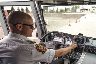A firefighter sitting in the drivers seat of a fire truck pressing buttons on the Command Zone screen next to the wheel.