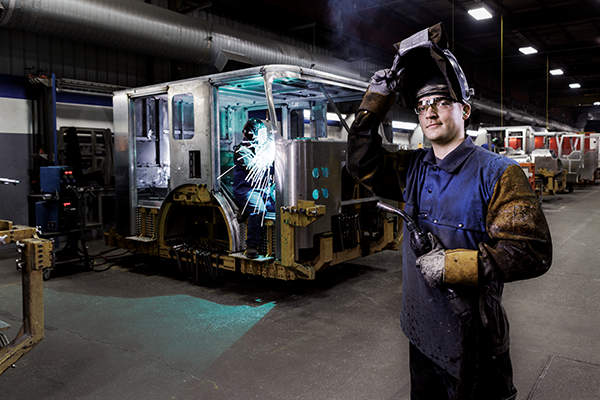 A welder standing inside of a warehouse next to a Pierce fire truck being assembled.