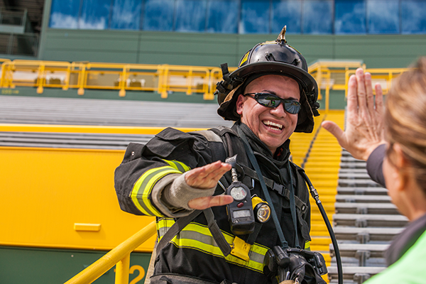 A Firefighter in turnout gear standing on the steps of Lambeau Field participating in the 9/11 Stair Climb event high fiving a woman.