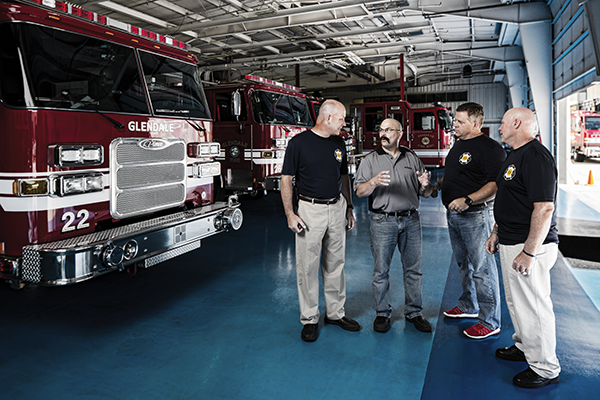 A Pierce Sales Representative and fire fighters standing on the blue floor near a Pierce Fire Truck.