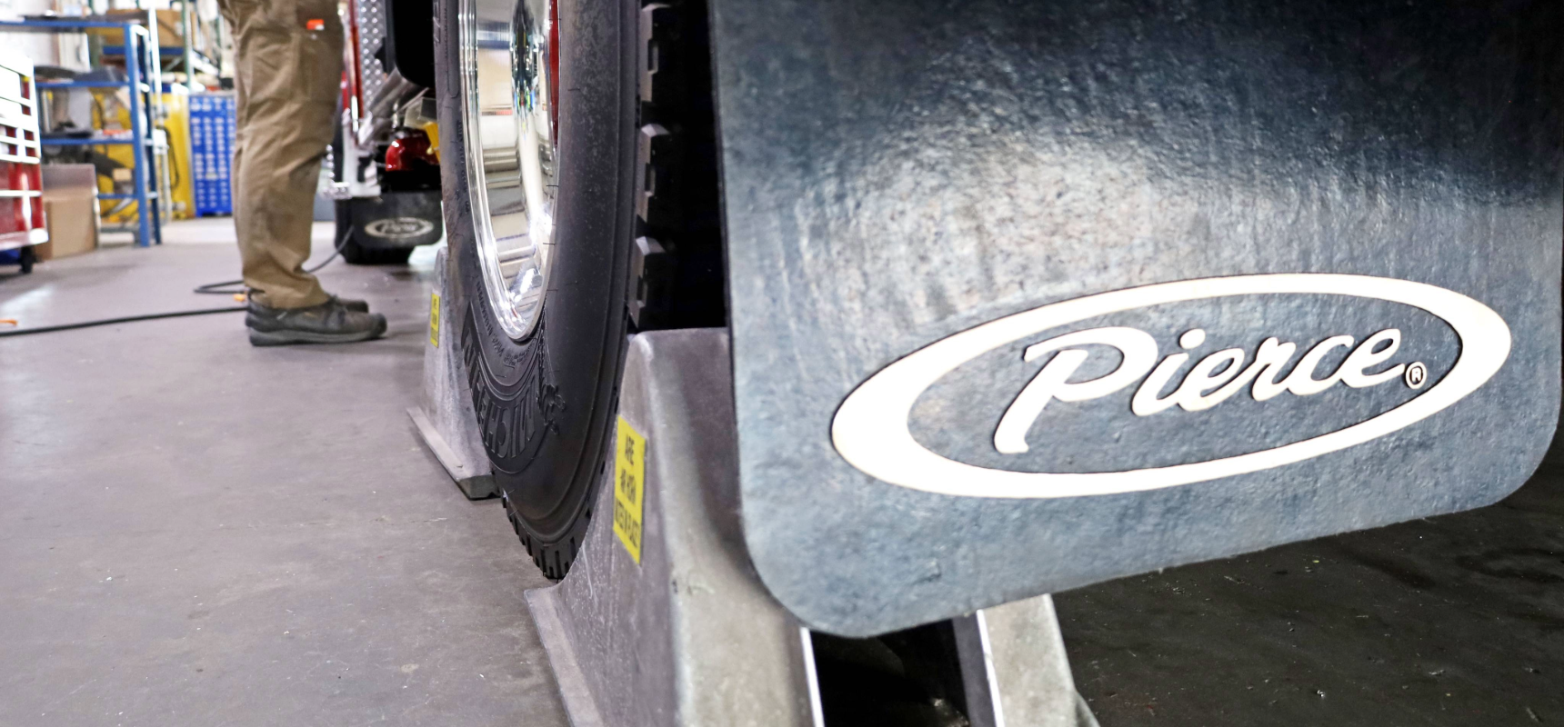 A Pierce tire flap in the foreground with a fire truck tire in chocks.
