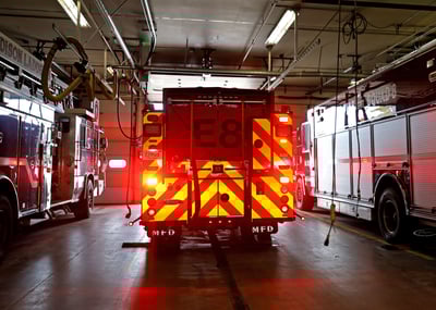 An electric fire truck is pulling out of a fire station bay with red lights visible with a red and yellow chevron pattern.