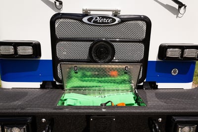 A green hose is visible inside of a white fire truck’s front bumper hose compartment.