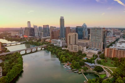 An aerial photograph shows Austin Texas, with the downtown area in the center and a river with two bridges in the foreground. 