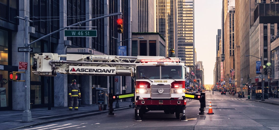 A mid-mount Ascendant aerial truck is posited with stabilizers engaged and the aerial device raised in the air in a city environment.