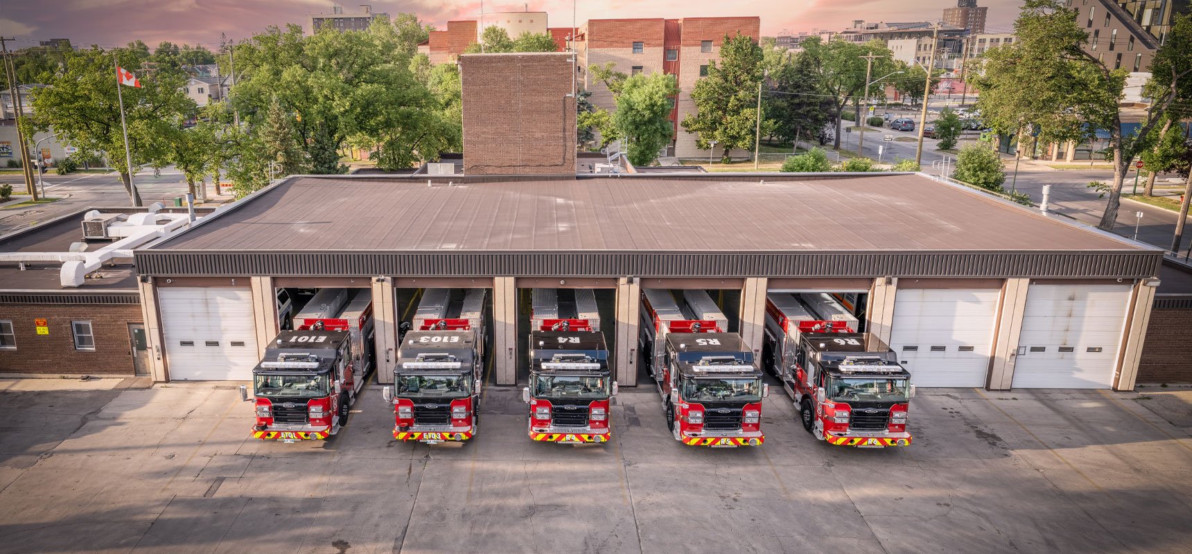 An aerial camera shows five Pierce fire trucks in Canada pulling out of an 8-bay fire station in unison. 
