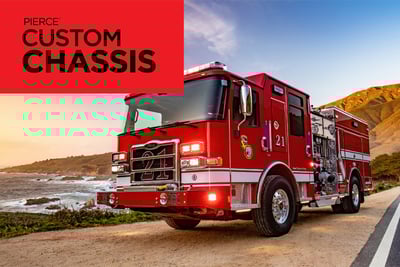 A red Pierce firetruck is parked on an angle next to a rocky mountain and oceanfront road. Pierce Custom Chassis is written in black on a red rectangle in the top left corner.