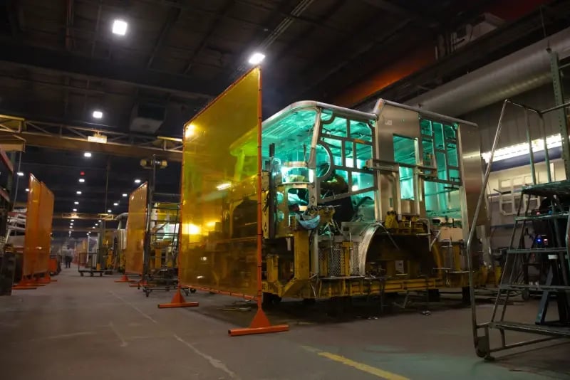 A technician welds a fire apparatus cab behind protective screens at a Pierce Manufacturing facility.
