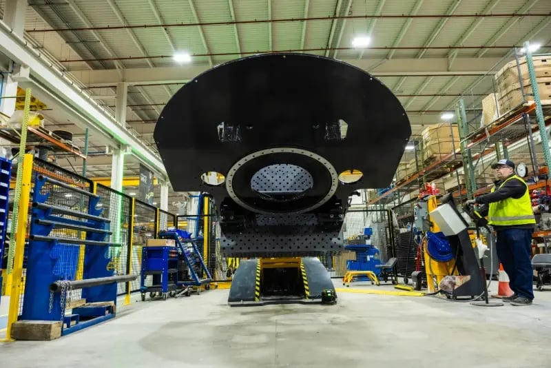 A worker operates a large weld positioner holding a heavy metal component inside a Pierce Manufacturing facility.