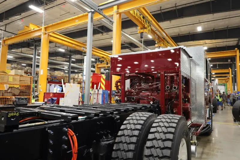 A fire truck chassis undergoing assembly with a red engine block in a Pierce Manufacturing facility.