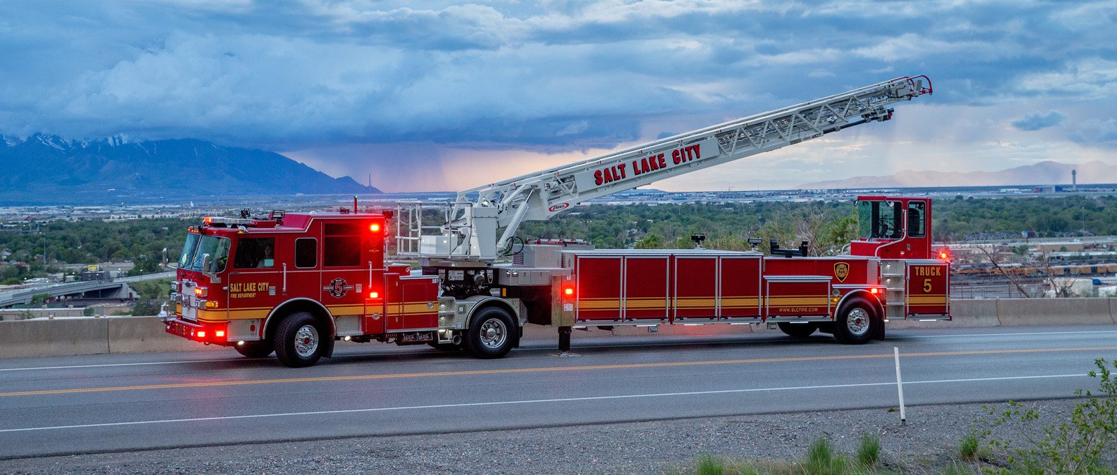 A red tiller truck is parked at sunset with its ladder raised in the air.
