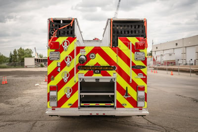 The rear end of the fire truck shows the folding steps to access the top, available storage and the required lighting and red and yellow chevron striping.