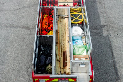 An overhead image of the top of a heavy duty rescue fire truck shows open hatch compartments with stored tools and equipment.
