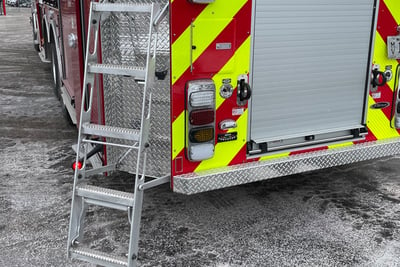 A mid-mount aerial fire truck is pictured with the rear platform access ladder deployed.