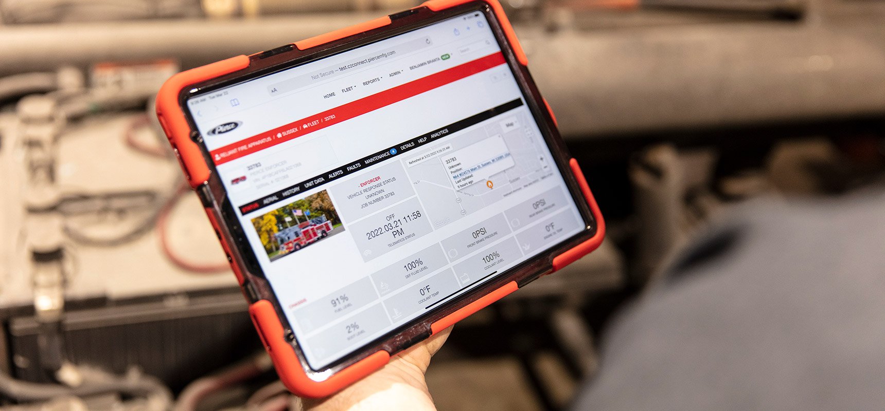 A hand holds an orange ipad case with fire truck telematics on the device screen. 