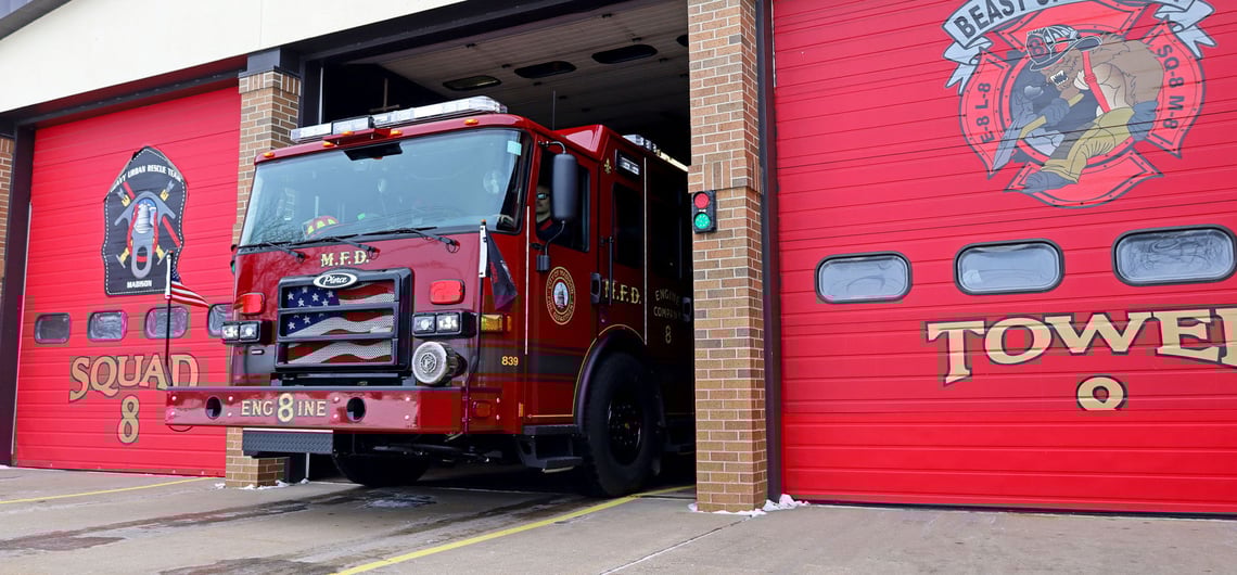 The red Pierce Volterra electric fire truck pulls out of The City of Madison Fire Department’s Station No. 8 from a bay door next to closed red bay doors. 