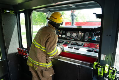 A firefighter operating controls inside the cab of a truck.
