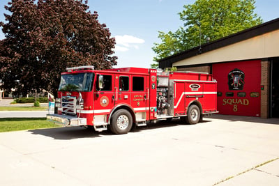 The red Volterra electric fire truck is parked outside of Madison Fire Department Station 8 with trees in the background. 