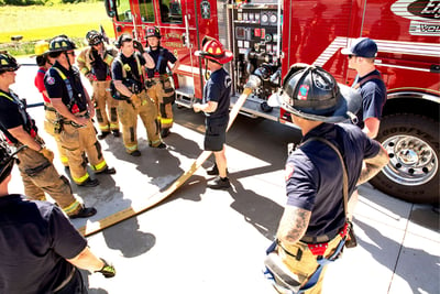 A group of firefighters in station gear talks standing next to the red Volterra electric fire truck. 