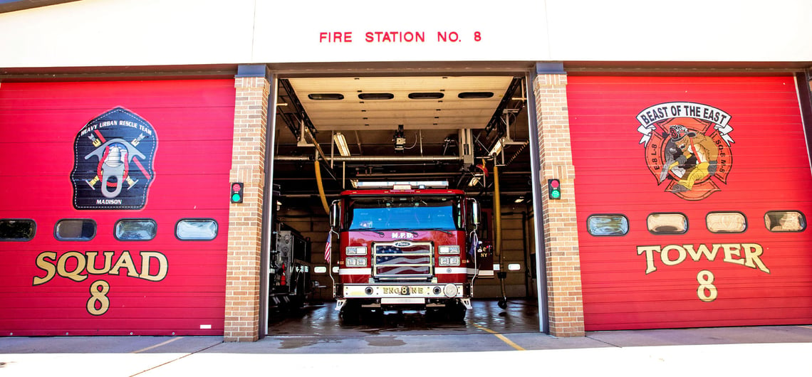 Madison Fire Station 8 has two red bay doors closed and one open with the red Volterra electric fire truck pulling out. 