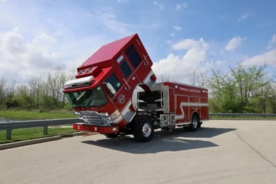 A red Pierce fire apparatus with its cab tilted forward, exposing the engine compartment for maintenance.