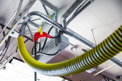 An overhead electric fire truck charging system is pictured in a fire station with a yellow diesel exhaust hose also visible. 