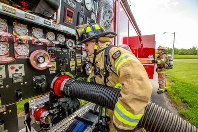 A firefighter connects a hose to the side panel of a Pierce fire truck.