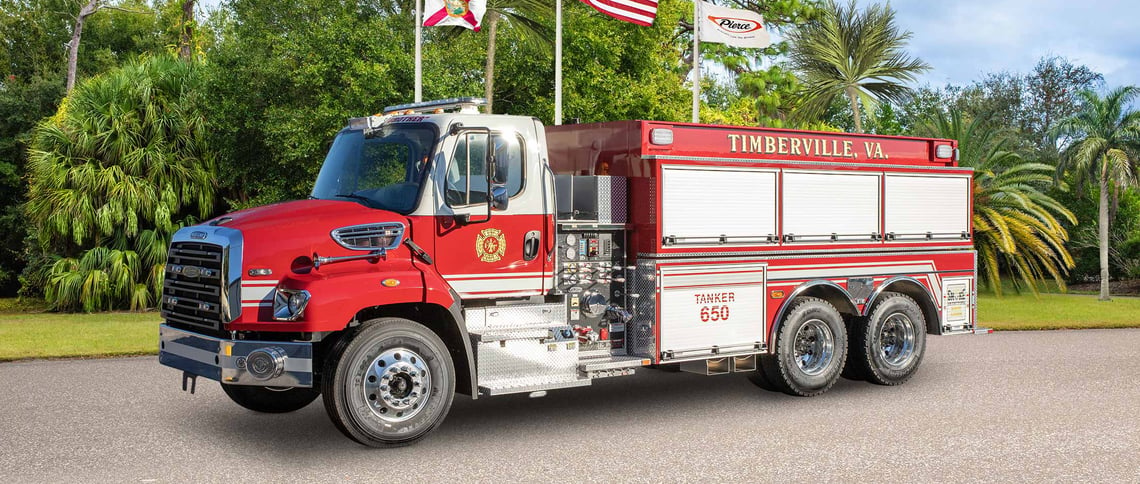The Timberville Volunteer Fire Department red and white tanker fire truck is parked on asphalt in a warm climate showcasing the driver side features.