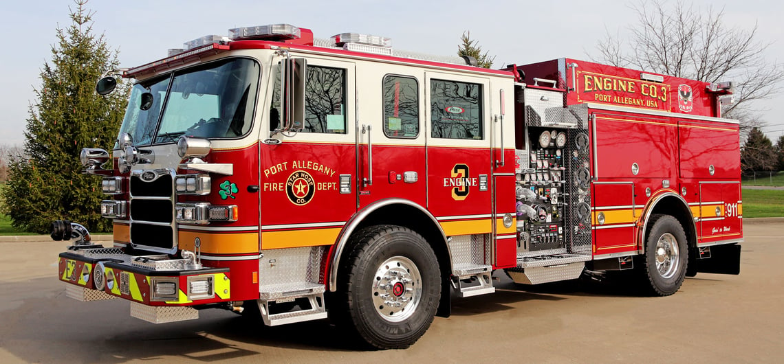 A red and white rural fire truck with a yellow stripe is parked on an asphalt road with trees and grass in the background.