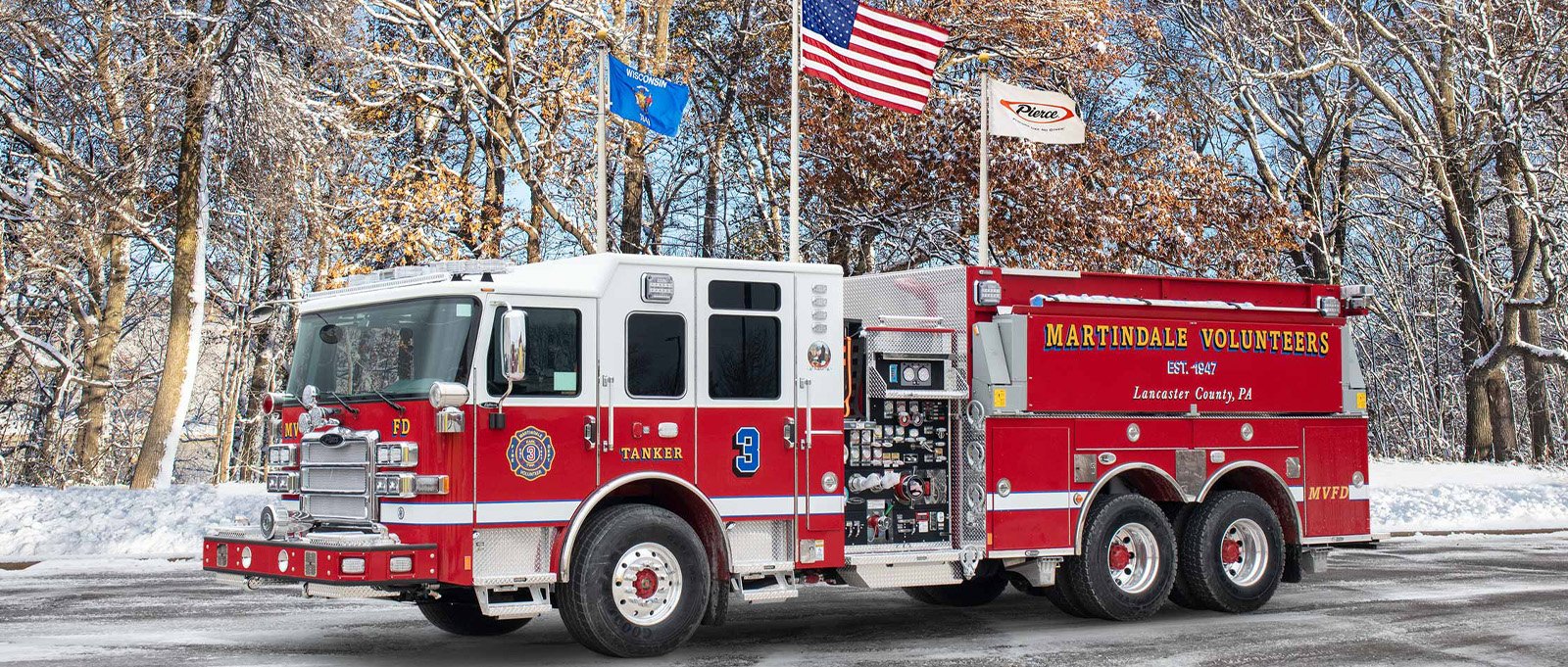 The Martindale Volunteer Fire Company red and white fire truck is parked on asphalt in a snowing setting showcasing the driver side features. 