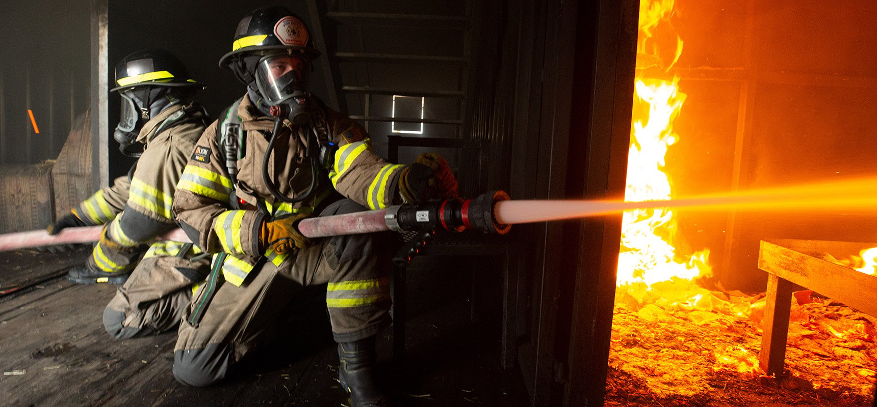 Two firefighters in full gear battle a blaze using a straight tip nozzle.