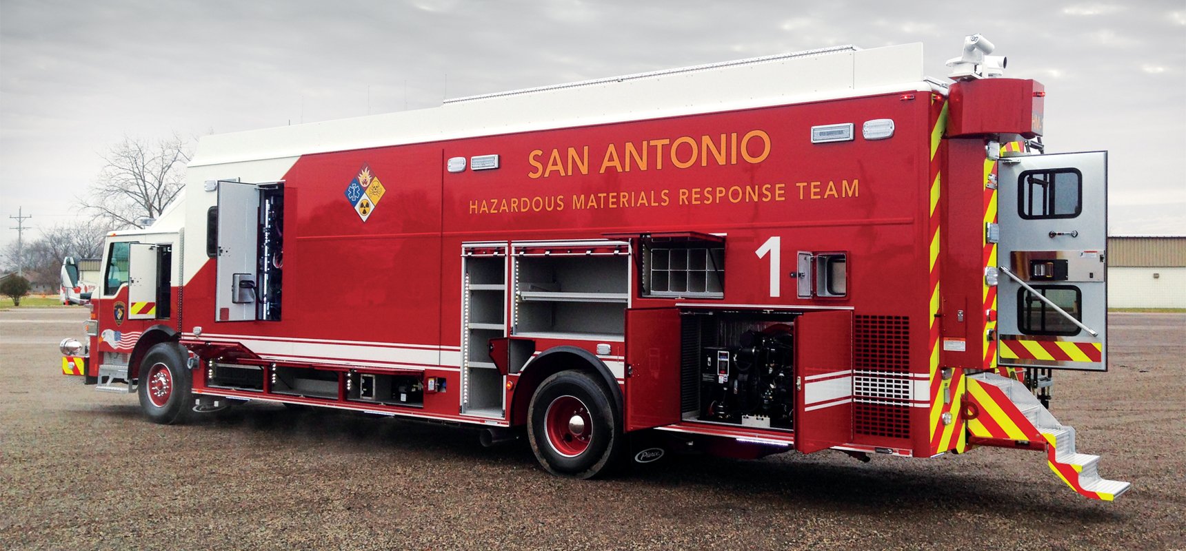 A red hazmat fire truck is parked with the compartments open to show the available storage space and equipment. 