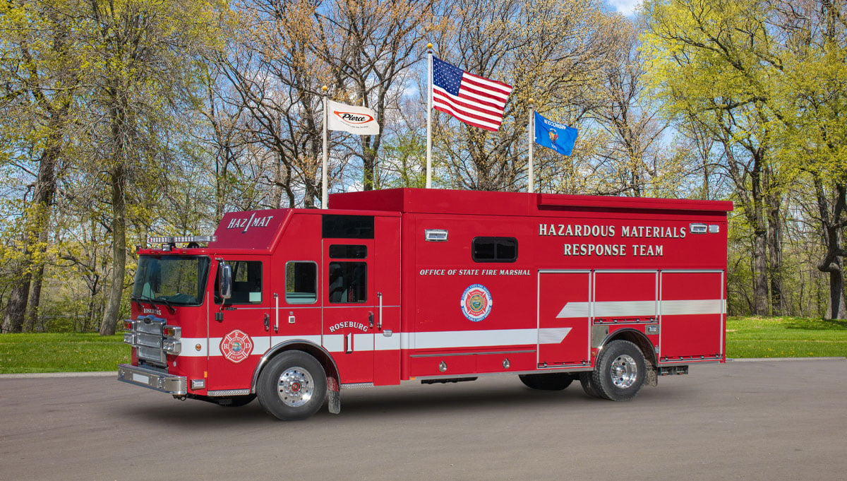 The red Oregon State Fire Marshal rescue is parked outside with three flags in the background. 