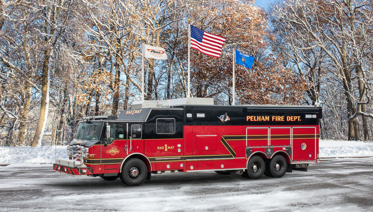 The red and black Pelham Fire Department combination hazmat rescue is parked with a winter background and three waving flags. 