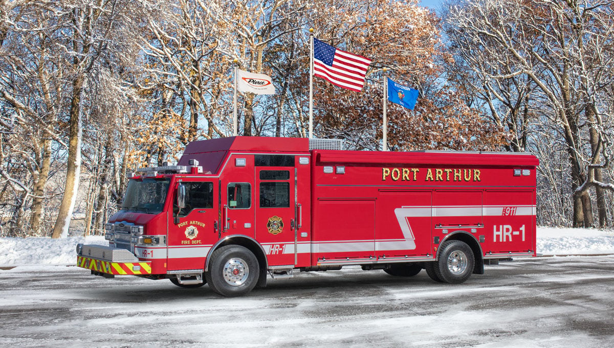 The red Port Arthur Fire Department combination rescue is parked showing the driver side with a winter background. 