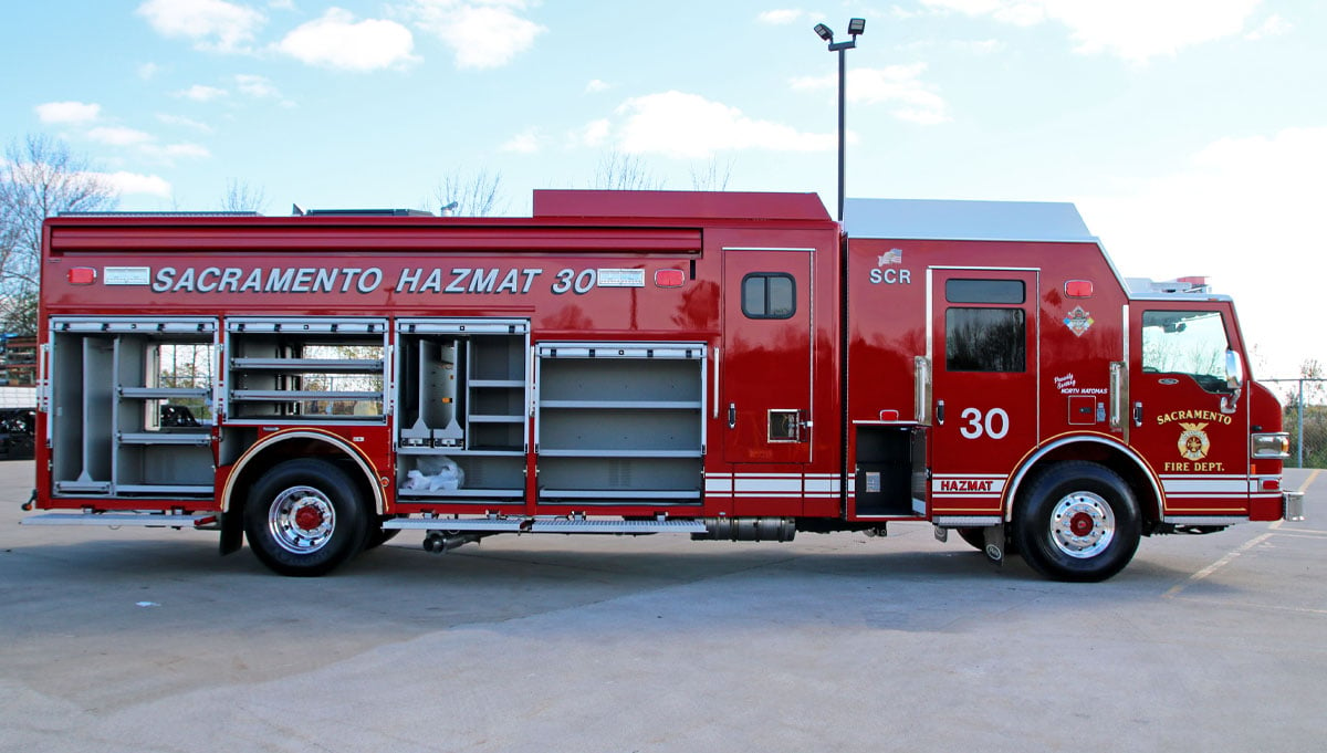 The Sacramento California Fire Department’s red combination rescue apparatus is pictured in a parking lot with the compartments opened to reveal storage. 