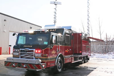 A red and black hazmat fire truck has two monitoring towers elevated above the truck as it sits parked outside in a snowy environment. 
