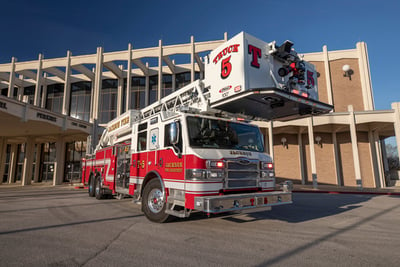 : A red and white fire truck is parked in front of a large office building with a blue sky background. 