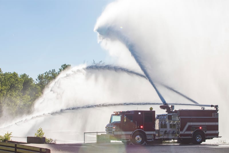 An industrial pumper truck is spraying water from three large nozzles in an outdoor setting.