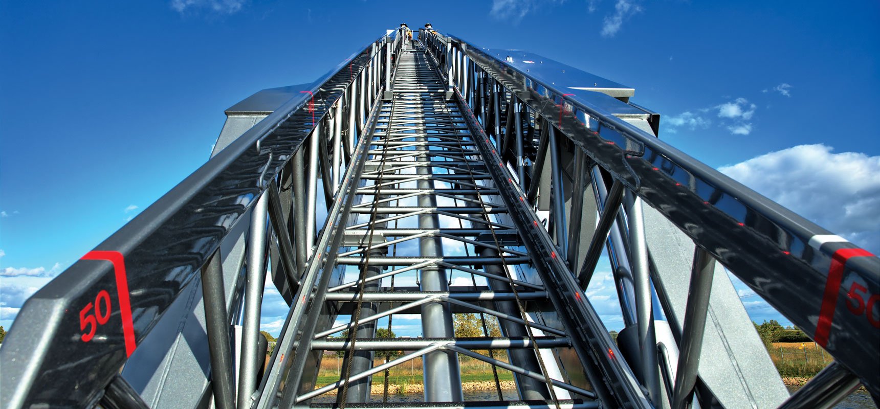An elevated aerial ladder is pictured extended up to a blue sky with clouds overhead.